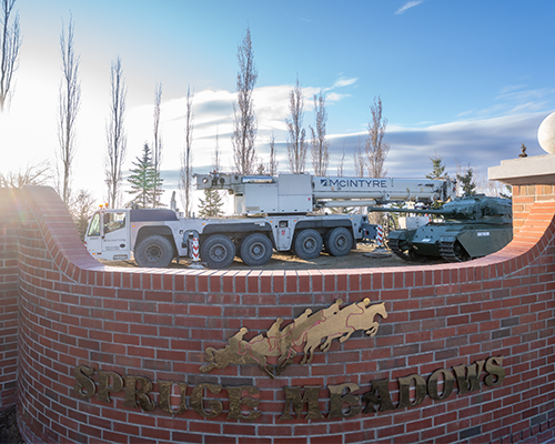 McIntyre mobile crane and military tank positioned behind the Spruce Meadows entrance sign on a clear day